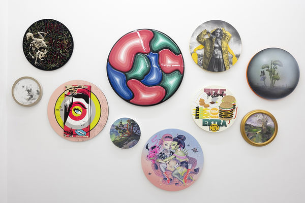 installation image of many round format artworks displayed on a white wall
