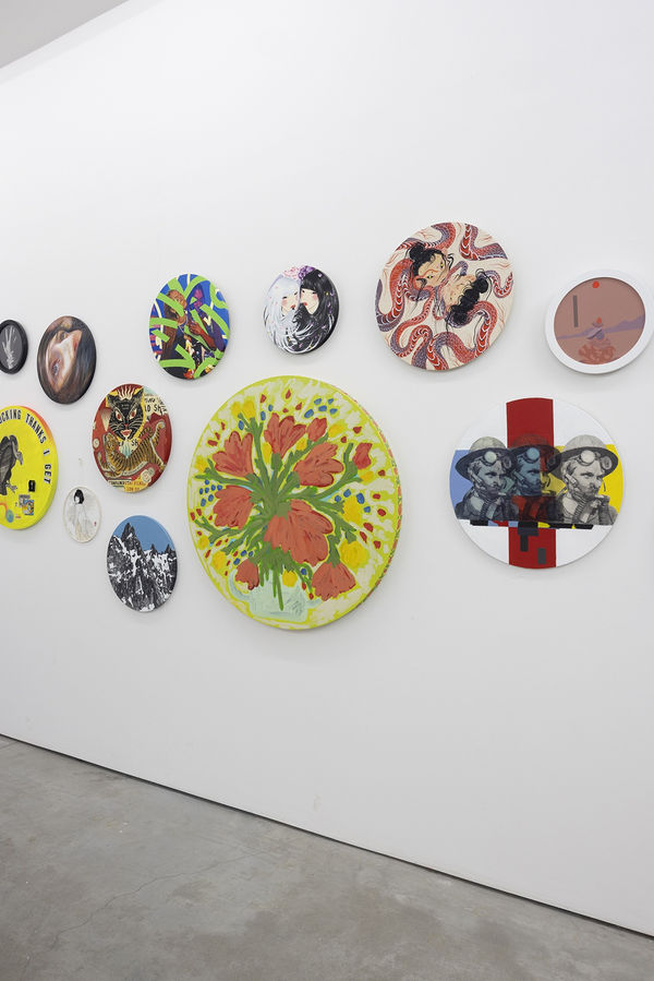 installation image of many round format artworks displayed on a white wall