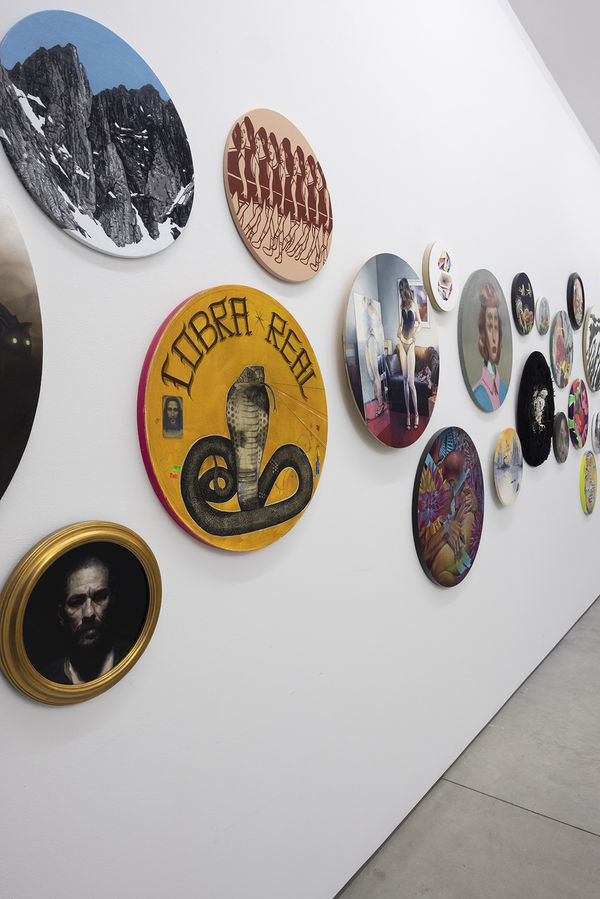 installation image of many round format artworks displayed on a white wall