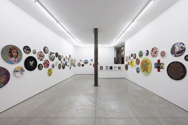 installation image of many round format artworks displayed on a white wall