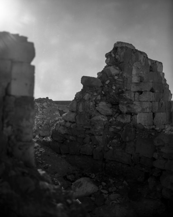 Close-up of crumbling ancient stone walls in a desert, with a blurred archaeological site in the distance under a hazy sky.