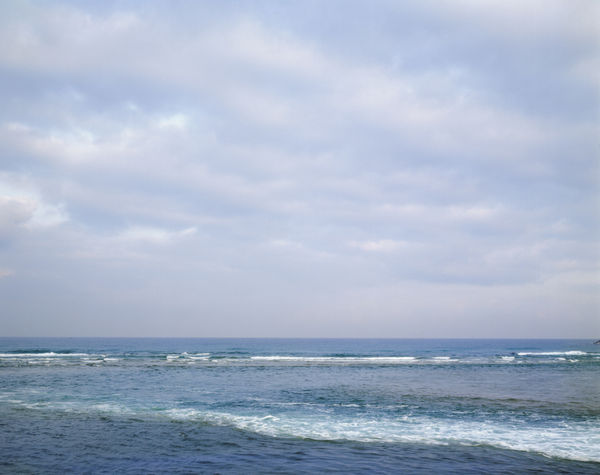A wide shot where the calm brown water of the Yarkon River meets the blue, crashing waves of the Mediterranean Sea.