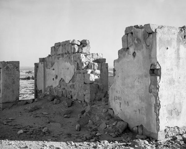 Stark black and white photo of ruined interior walls with faint Hebrew inscriptions and modern markings on the plaster.