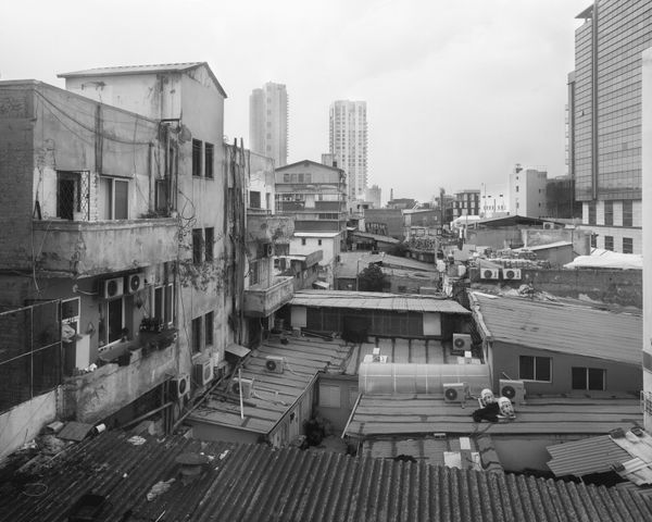 Wide B&W urban landscape by Ariel Yannay. Rooftops, air conditioners, and distant skyscrapers of Tel Aviv under a soft, overcast sky.