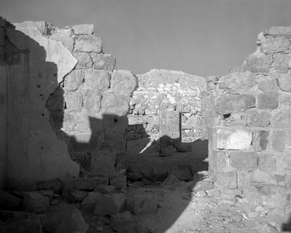 Deep shadows cast across a crumbling stone courtyard in the desert, creating a high-contrast geometric pattern.