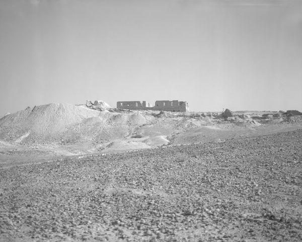 A high-key monochrome photo of a weathered stone building sitting on a bright desert plateau.