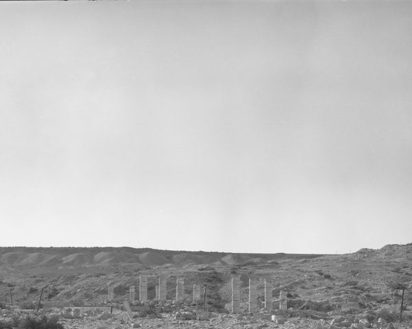 A row of weathered stone pillars standing in a desolate desert landscape under a vast, empty sky.