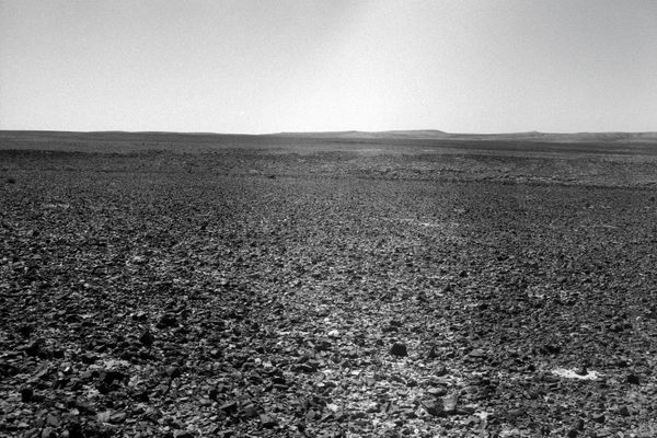 Ariel Yannay: The Mountain of God 10. A vast expanse of nuanced stones under a bright sky, emphasizing the stillness and lingering presence of the site.