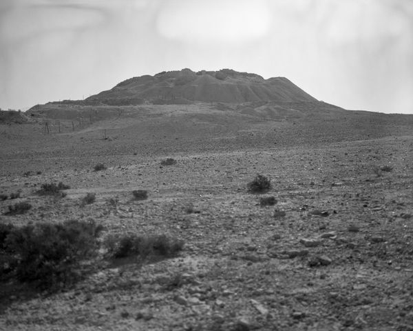 A wide-angle view of a rocky desert plain leading to a distant hill topped with the faint remains of ancient structures.
