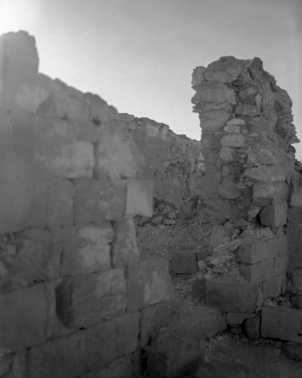 Close-up of eroded, light-colored stone walls with jagged edges against a pale, high-key sky.