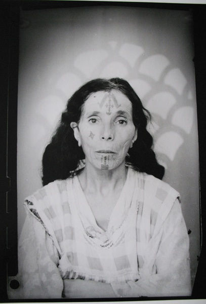1960s black & white portrait of Amazigh woman with facial tattoos, wearing white dress, in a photography studio