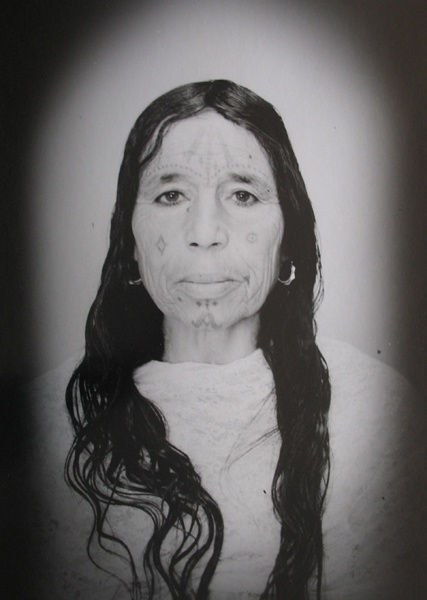 1960s black & white portrait of Amazigh woman with facial tattoos, wearing white dress, in a photography studio