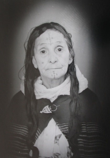 1960s black & white portrait of Amazigh woman with facial tattoos, wearing white dress, in a photography studio