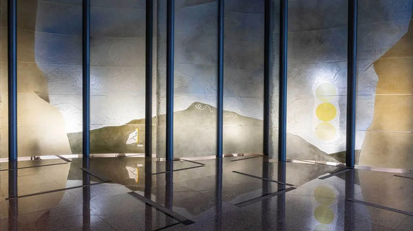 Large dichroic glass sculpture like an oversize modular screen (green, yellow, blue) with two people next to it