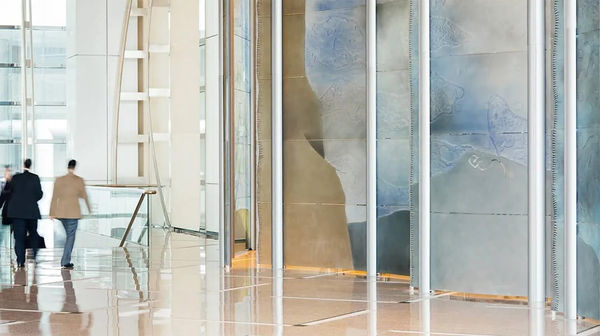 Large dichroic glass sculpture like an oversize modular screen (green, yellow, blue) with two people next to it