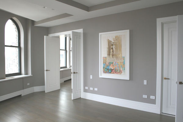 An interior room painted in light beige with dark wood herringbone flooring. Artwork hangs on the walls.