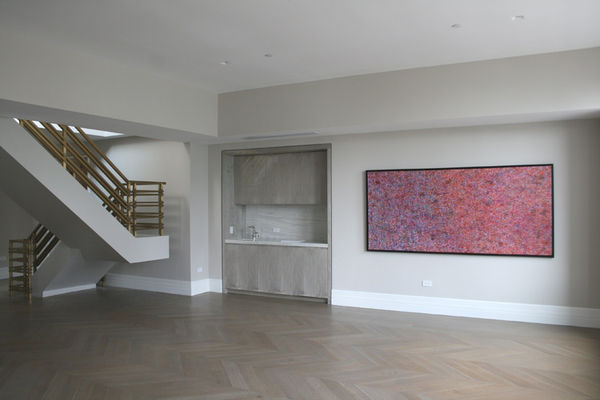 An interior room painted in light beige with dark wood herringbone flooring. Artwork hangs on the walls.