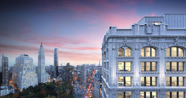 Exterior photograph of a Beux-Arts building on the right with the skyline of New York City on the left at sunset.
