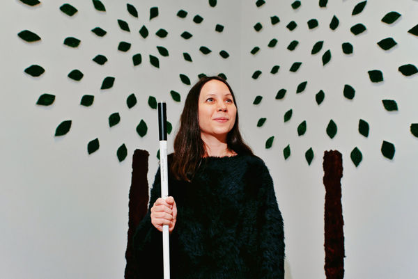 Artist Emilie L Gossiaux poses with her white cane in front of her Queens Museum exhibition