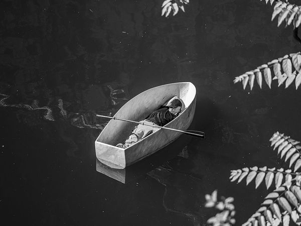 Man lying inside a marble boat floating on water, seen from above, artwork by Fabio Viale. Photograph by Laura Veschi.