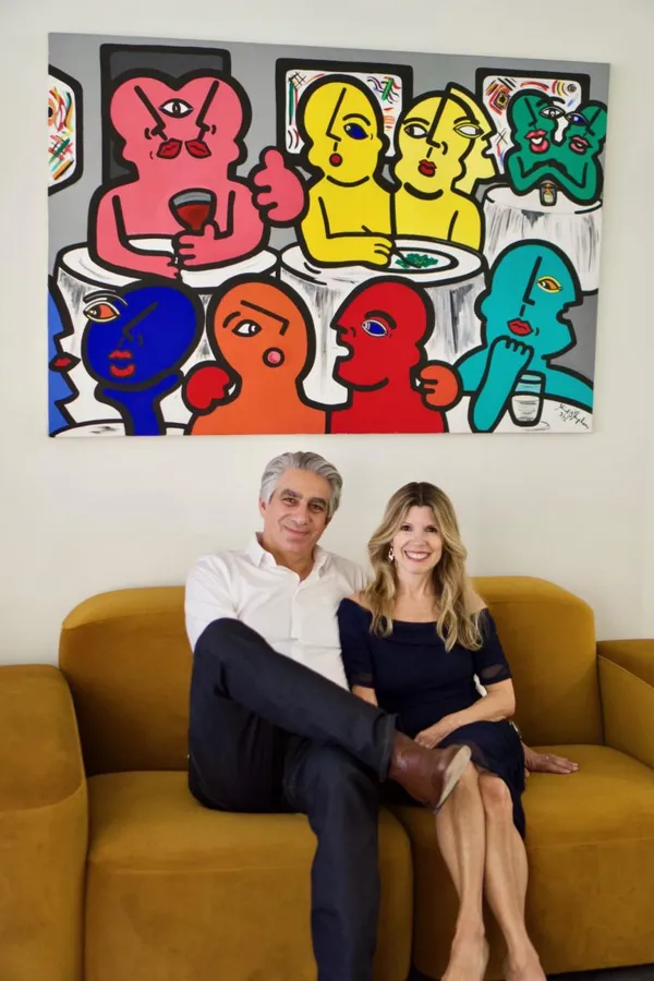Steven and Ana Soulios sitting in front of a painting by Heidi Stephens (Photo courtesy of Soulios Gallery)