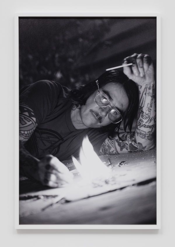 Close up of the artist Pig Pen prone on the ground lighting a small fire with matches in front of him