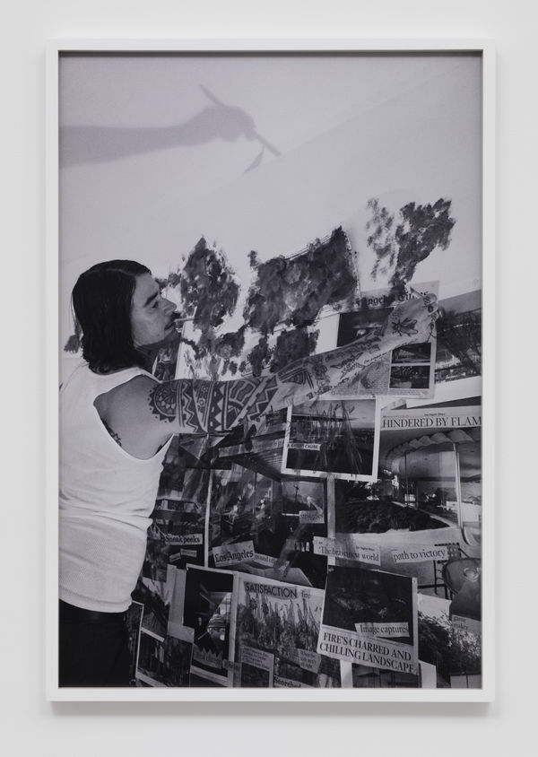 The artist Pig Pen on a step ladder attaching photographs to a wall collage.