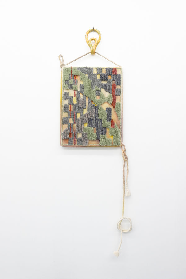 Textile work with an abstract pattern. The textile is stretched and hanging on a handmade ceramic hook.
