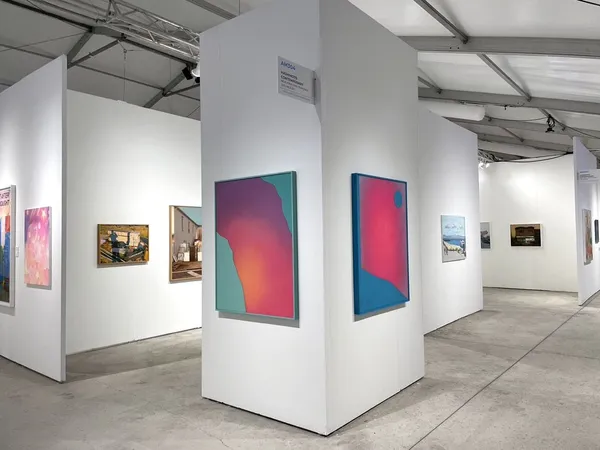 Photo of colorful paintings hanging on white walls in a booth at an art fair