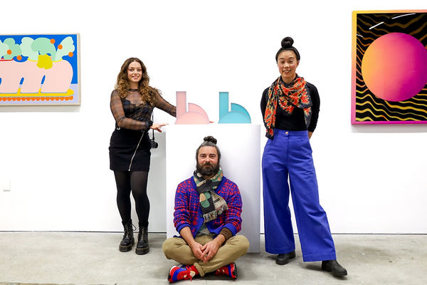 CHIAOZZA and Rachel Strum at the opening of their exhibition "Cosmic Bloom" inside a white wall gallery, standing and sitting among their sculptures and paintings.