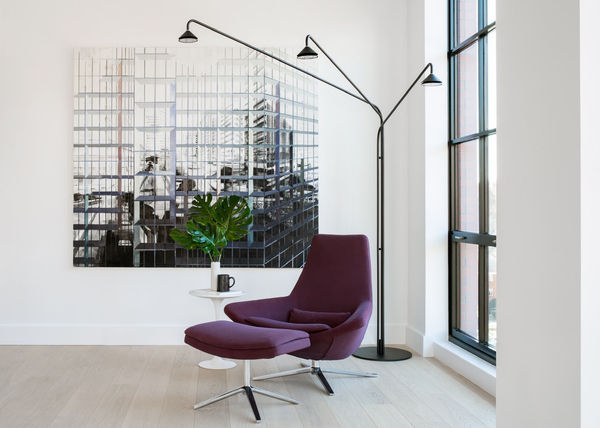 Maroon lounge chair with matching ottoman and thee tiered floor lamp with large painting by Driss Ouadahi.