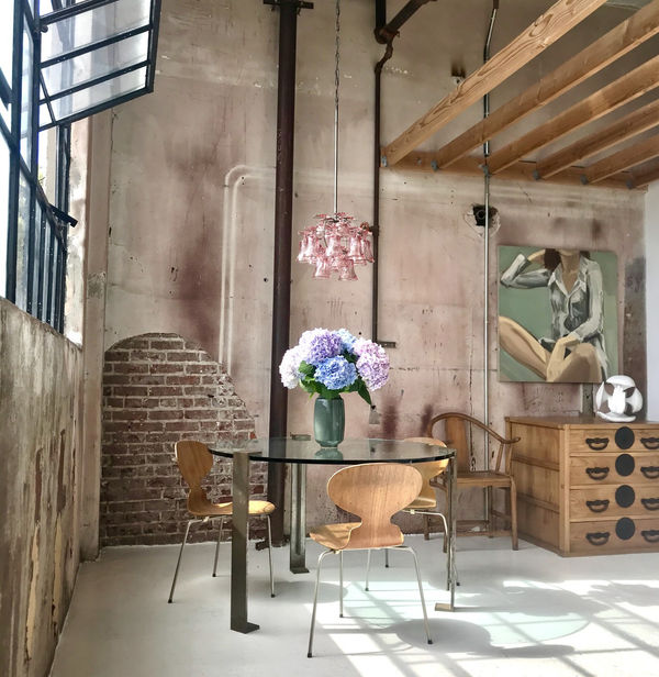 Hosfelt Gallery with glass table and wooden chairs with Wooden Japanese tonsu. A large painting of woman sitting down and a white humanoid sculpture by Tim Hawkinson sit above the tonsu or chest of drawers.