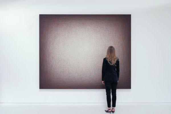 Woman standing in front of rectangular, dark maroon thread painting by Emil Lukas.