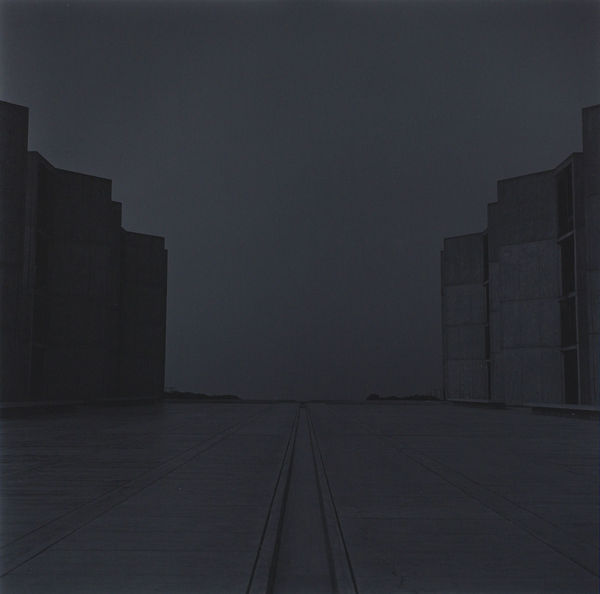 photograph of road between two buildings, one dark and one light, at night with no lights