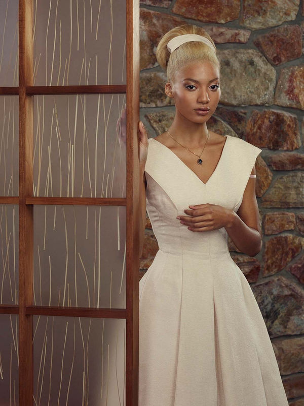 woman in pink dress with bra strap over shoulder looking at viewer from beside a room divider