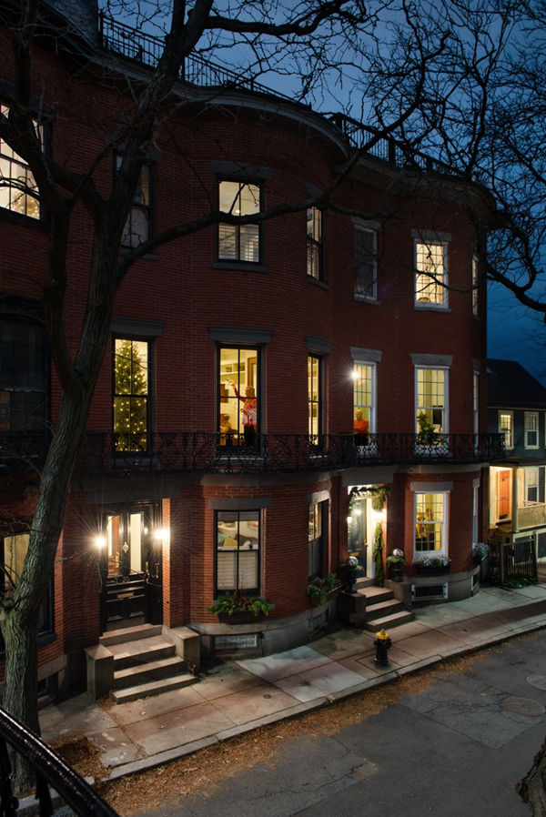 Brick apartment building in Boston from across the street, with domestic scenes in each window, including a lit Chrsitmas tree, a woman decorating, and a man sitting at the table, by Gail Albert Halaban