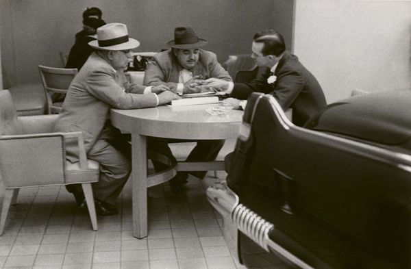 three white men in suits and hats sitting around a round table in a Cadillac showroom with the rear fin of a Cadillac in the foreground as if the fourth person at the table, by Robert Frank