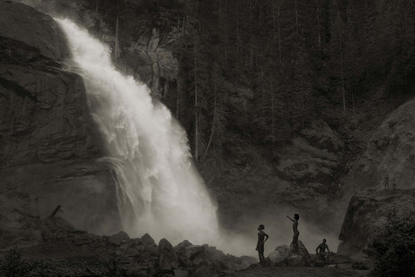 Erwin Olaf photograph of nude figures standing near a waterfall in a forested landscape, captured in black and white with dramatic lighting and mist