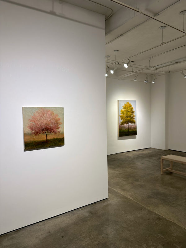 Photo of an installation with two paintings visible. They are of trees, framed symmetrically in the center of the canvases.