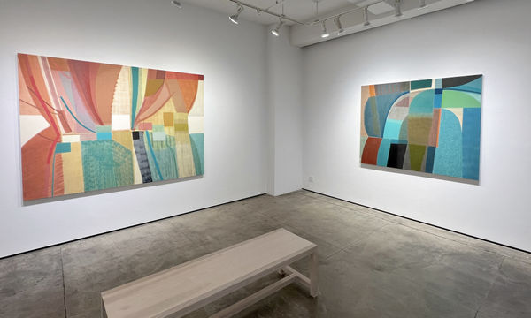 exhibition with two large geometric abstract oil paintings, cool in tone, are on the walls. there is a bench in the center of the room