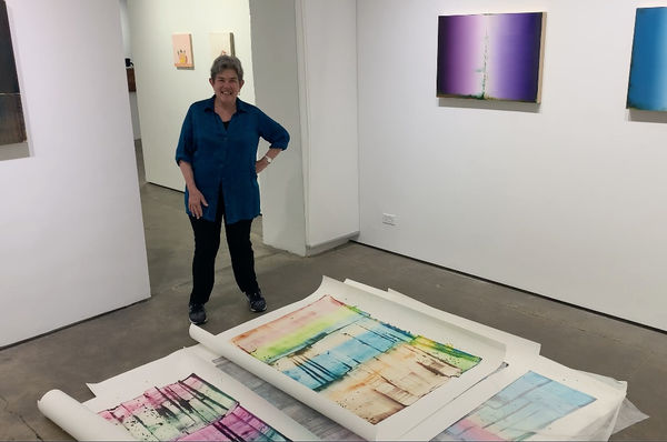 Kathy Markel standing with paintings by Sarah Irvin