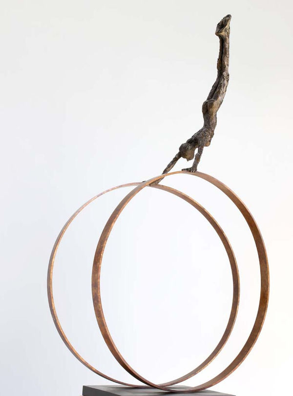 Carol Peace sculpture of a small figure in bronze seen upside down holding two circles, swinging their body between them like a gymnast.
