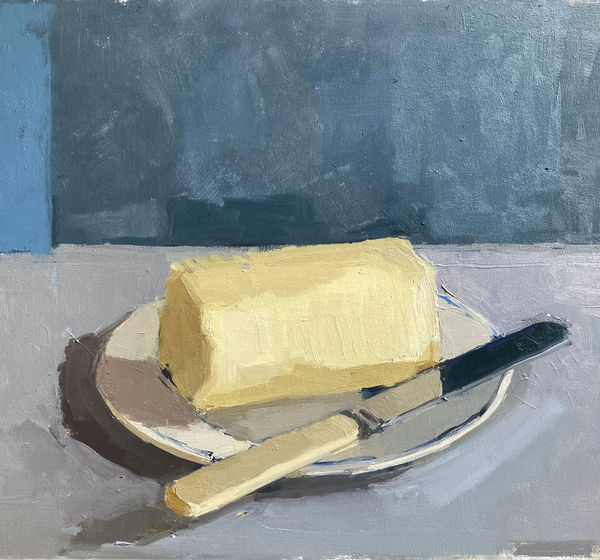 Sarah Spackman still life painting of a block of butter arranged with a butter knife besides it, painted in figurative brush strokes. The block is resting on a small white dish. The surface is a pale grey and the wall in the background steel coloured.