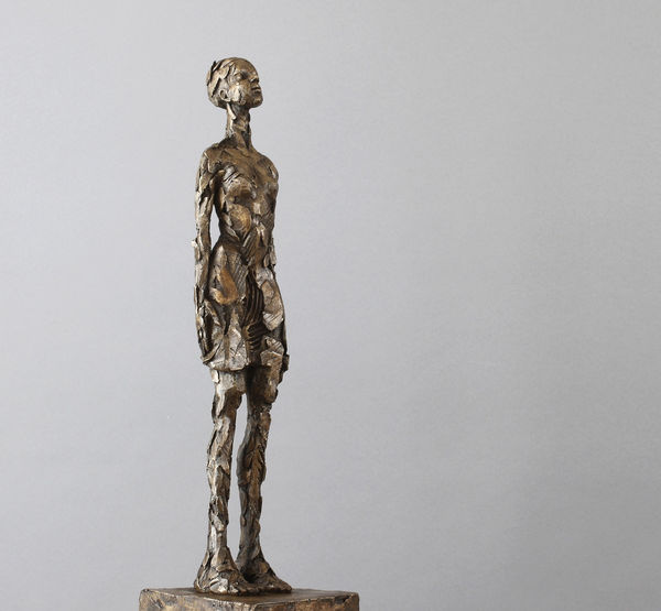 Carol Peace, roughly textured sculpture with of a woman standing straight with head slightly lifted, wearing a short dress and wearing her hair in a bun.