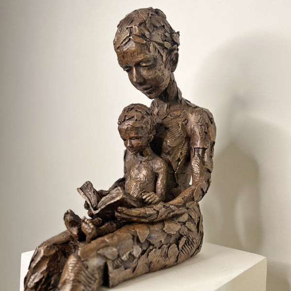 Carol Peace sculpture of a female figure holding a child on her lap reading a book in bronze resin