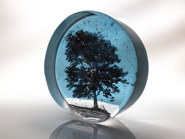Helen Slater glass art piece in blue with the dark silhouette of a tree.