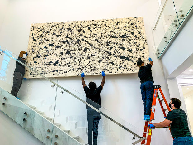 People installing artwork purchased from art gallery Carousel Fine Art in art collector's home.