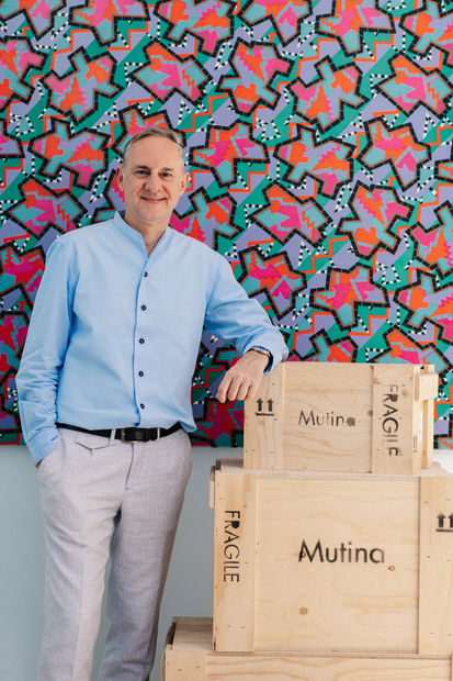 Portrait of Olivier David, Director of OFFMARKET Gallery, standing beside stacked Mutina art crates in front of a colourful Memphis-style artwork.