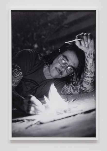 Close up of the artist Pig Pen prone on the ground lighting a small fire with matches in front of him