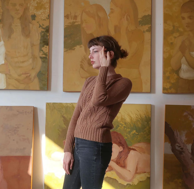 photograph of Rachel Gregor standing in front of a group of her paintings on a wall